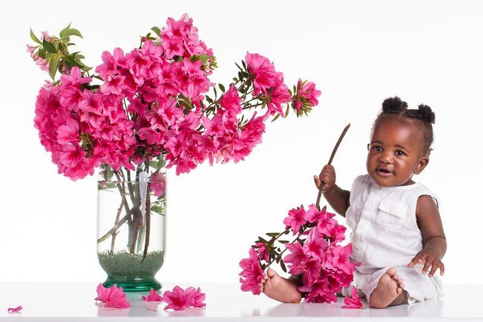 Little girl holding a pink flower bunch sitting next to a flower vase.