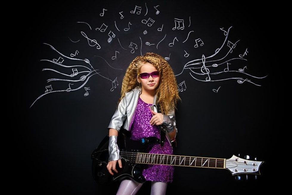 Little rock star singing with her electric guitar over musical background