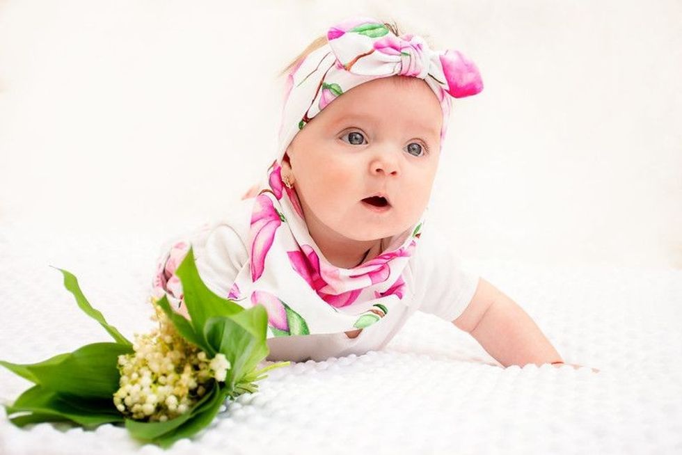 Newborn baby girl crawling on floor next to flowers.