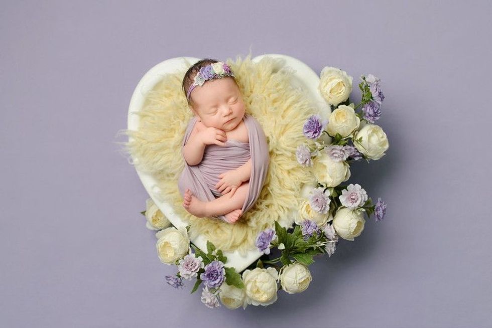 Newborn baby sleeping in a furry basket with white and lavender flowers.