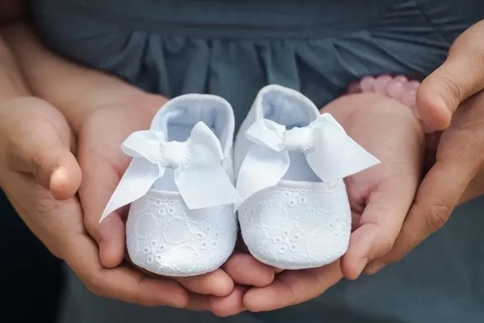 Parents holding a pair of white baby girl shoes