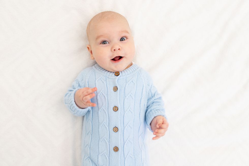 portrait of a baby boy in light blue coverall on the bed.