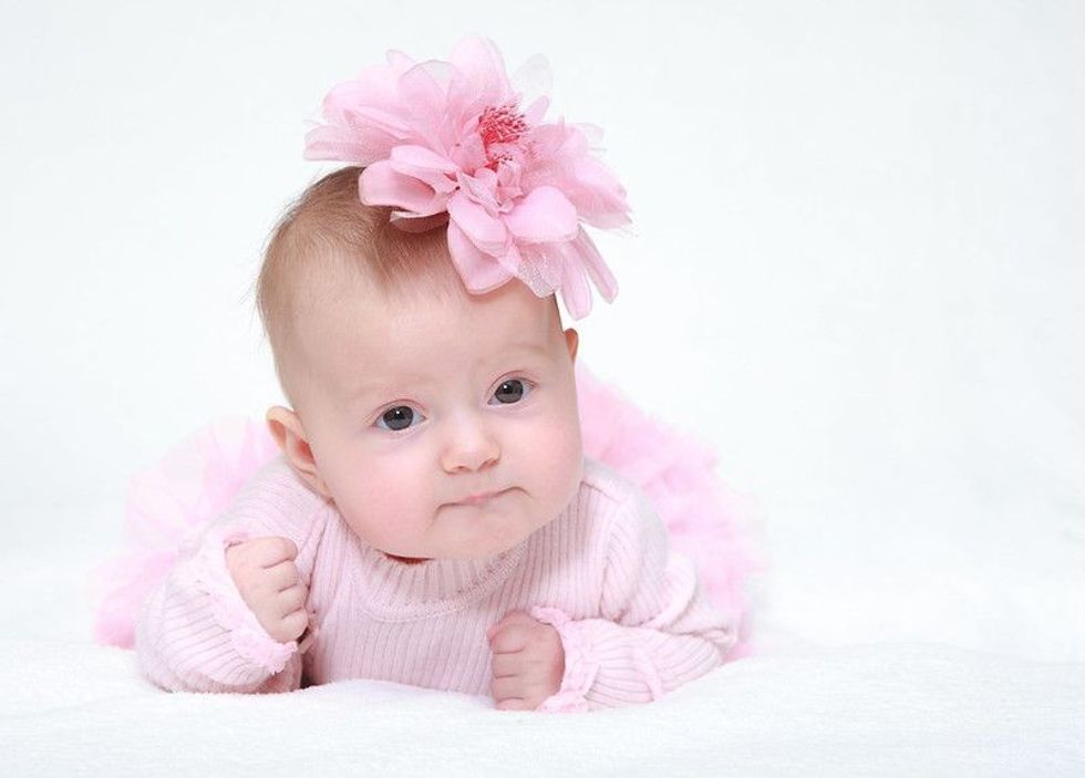 Portrait of a baby girl with a flower on her head on a white background.