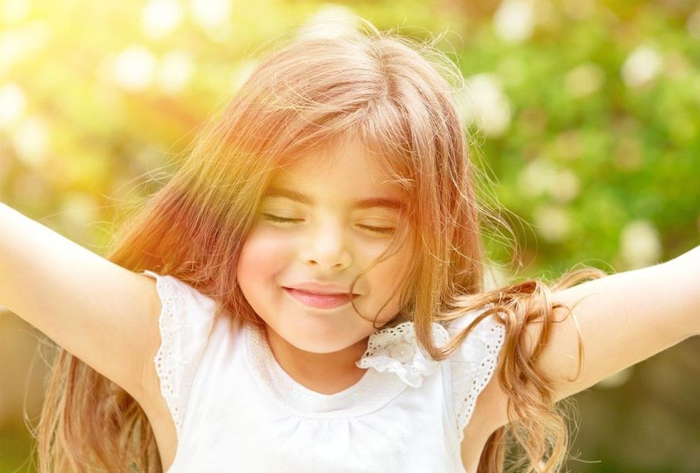 Portrait of attractive little Arabic girl with closed eyes enjoying sunny day