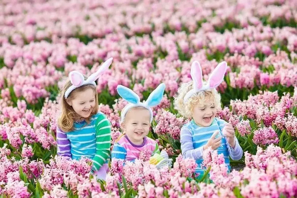 Three girls wearing bunny ears are sitting in pink flower garden