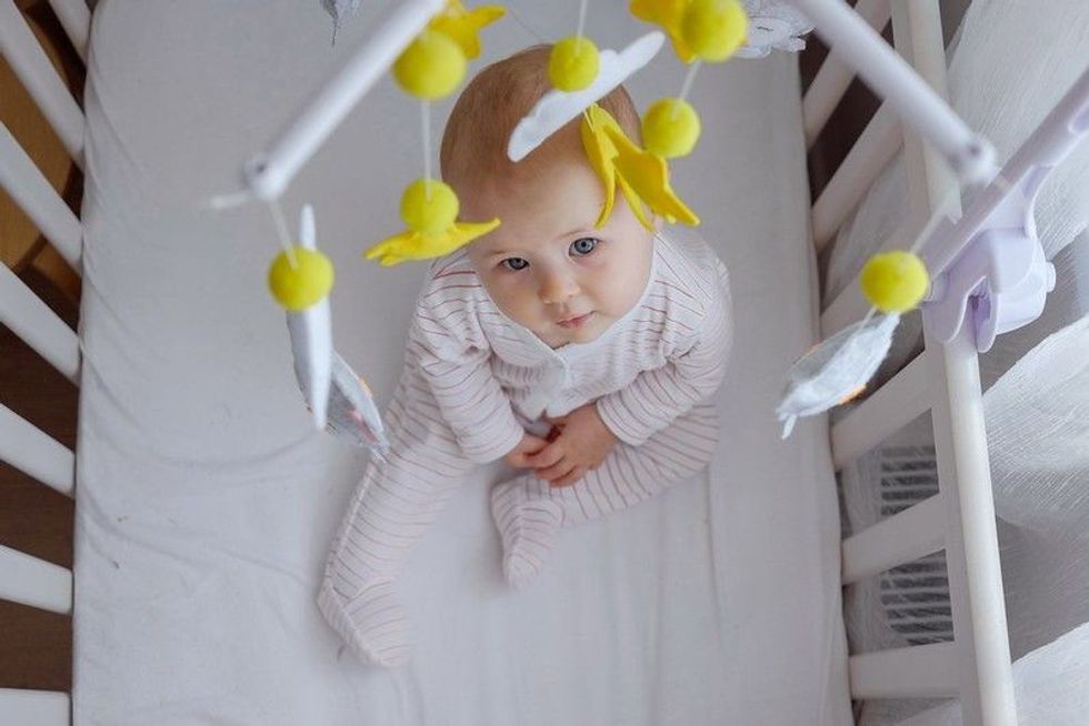 Top view of a baby sitting in crib and looking at hanging mobile.