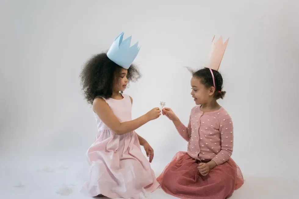 Two little girls wearing pink and blue crowns are playing with each other