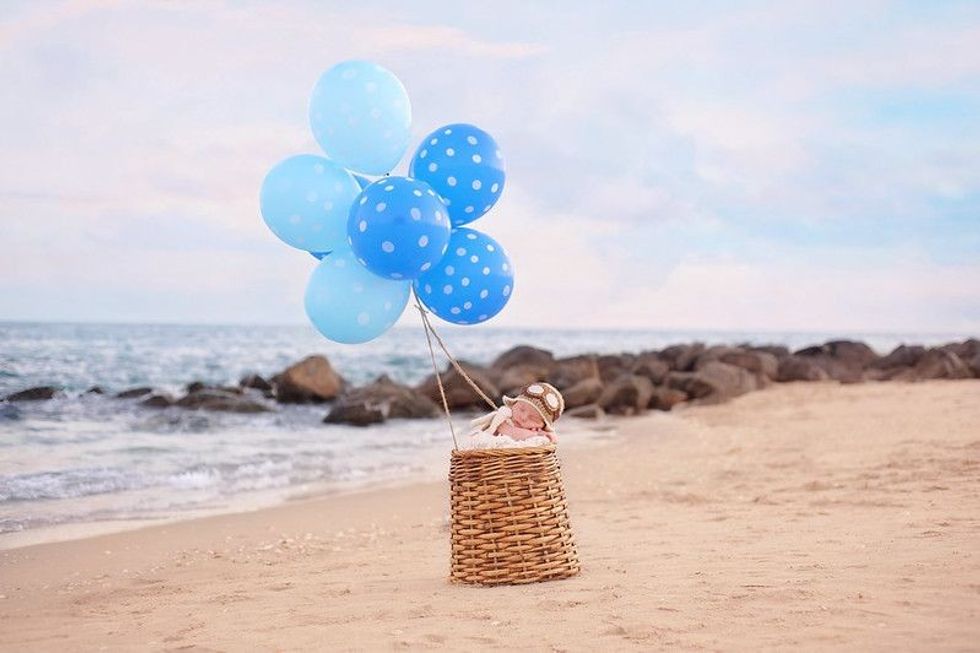 Two week old newborn baby boy sleeping in a wicker basket with blue balloons