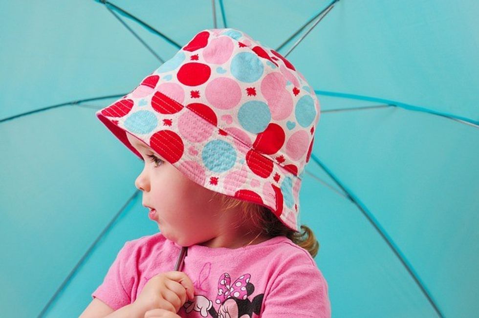 Young girl in a patterned hat under a blue umbrella.